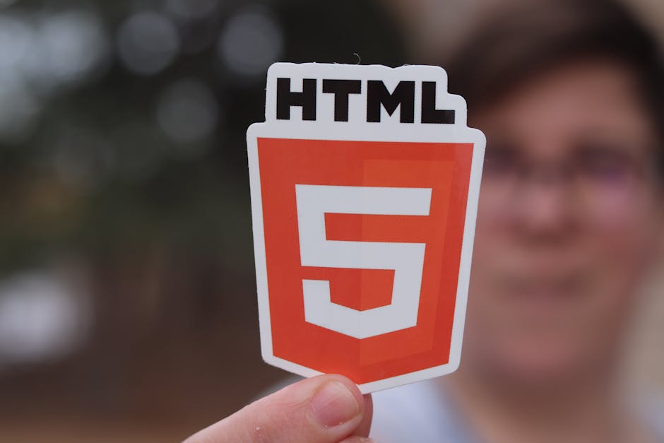 A person holding a card with the HTML5 logo outdoors, in front of a blurred background with trees and a building, representing modern web technologies. The card displays a red shield icon with a white